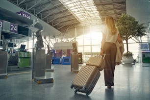 Attentive female person carrying her luggage and going to the necessary gate for taking her sit in plane