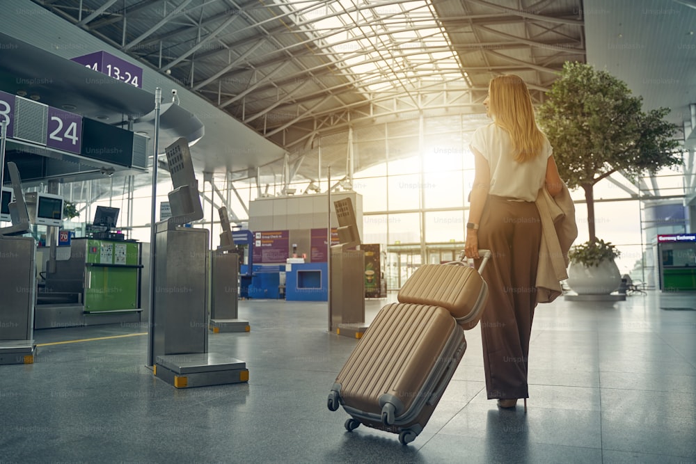 Aufmerksame weibliche Person, die ihr Gepäck trägt und zum notwendigen Gate geht, um sie im Flugzeug zu sitzen