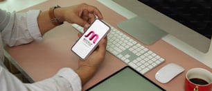 Cropped shot of male hands using mock up smartphone on office desk with digital devices and coffee cup