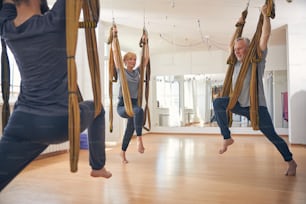 Three people doing an aerial warrior two pose using a silk hammock at a gym