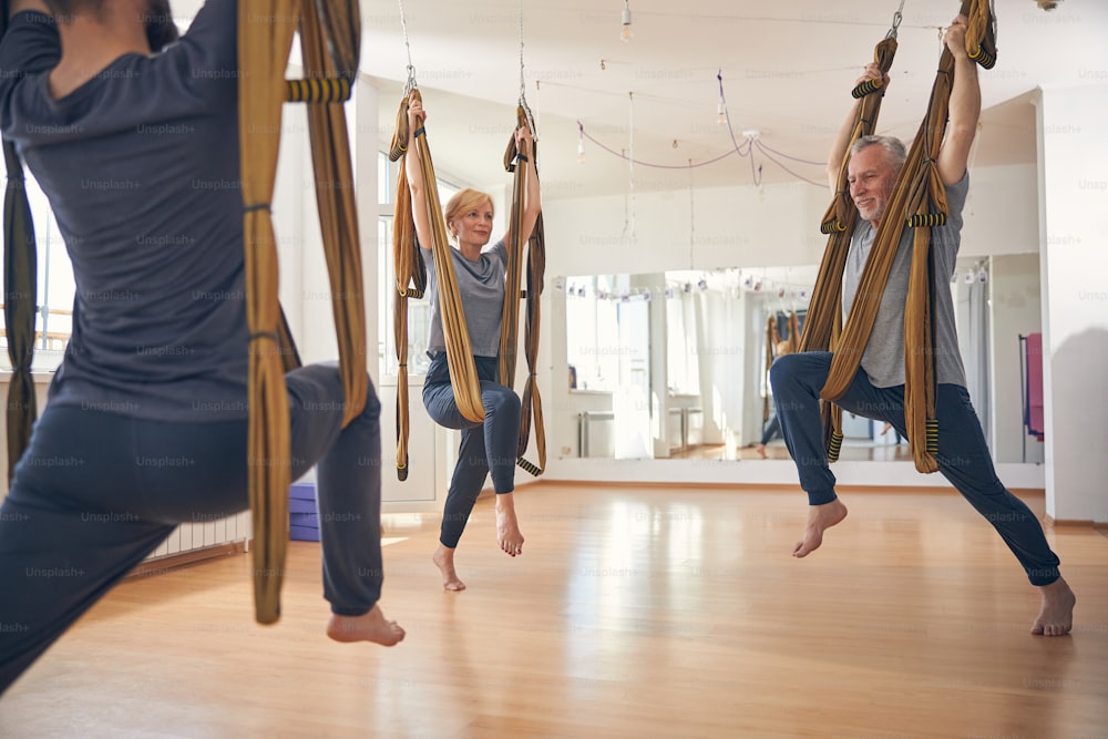 Three people doing an aerial warrior two pose using a silk hammock at a gym