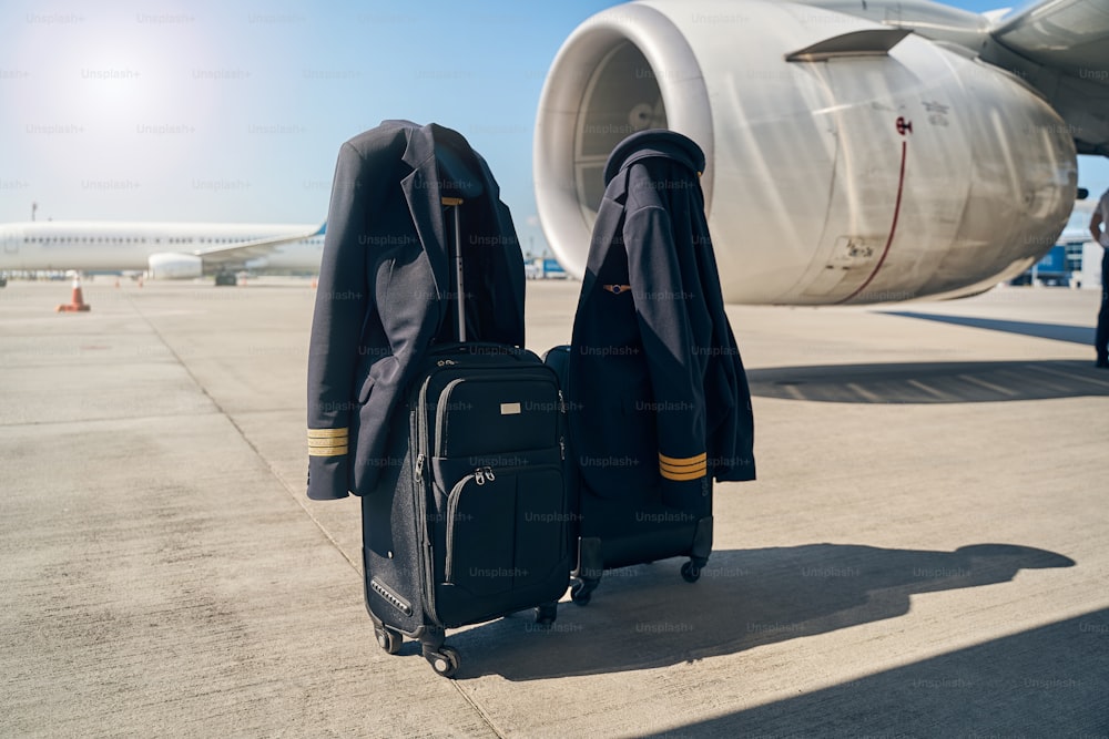 Two pairs of jackets and caps hanging on the retractable luggage handles by an airplane