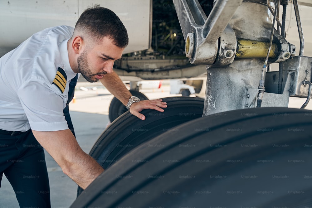 Aviador qualificado de cabelos curtos focados em uniforme verificando o sistema de trem de pouso do avião antes do voo