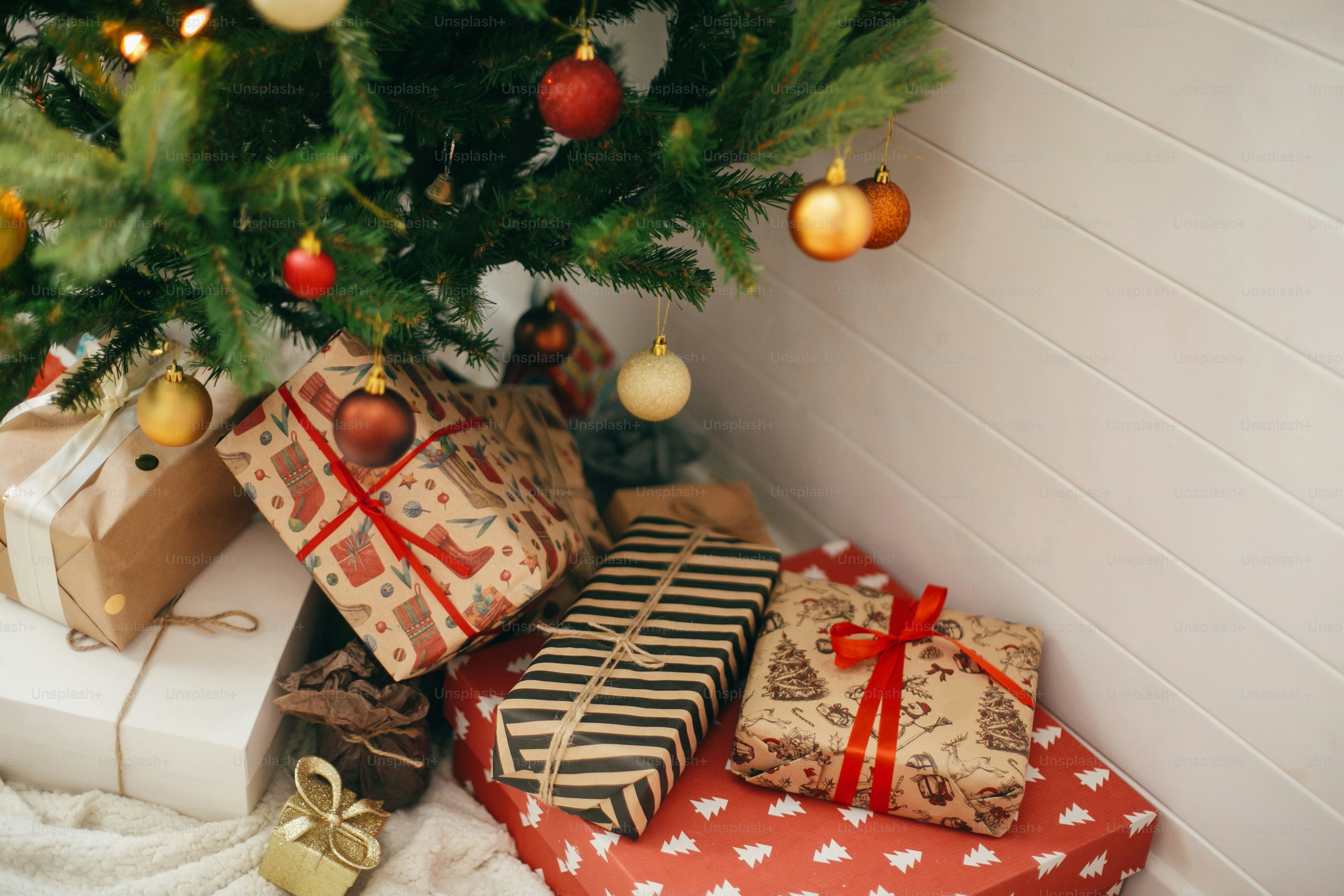 Frohe Weihnachten. Stilvolle Weihnachtsgeschenke unter dem Weihnachtsbaum mit roten und goldenen Kugeln. Geschenke in handwerkliches modernes Papier im festlichen skandinavischen Raum verpackt. Platz für Text