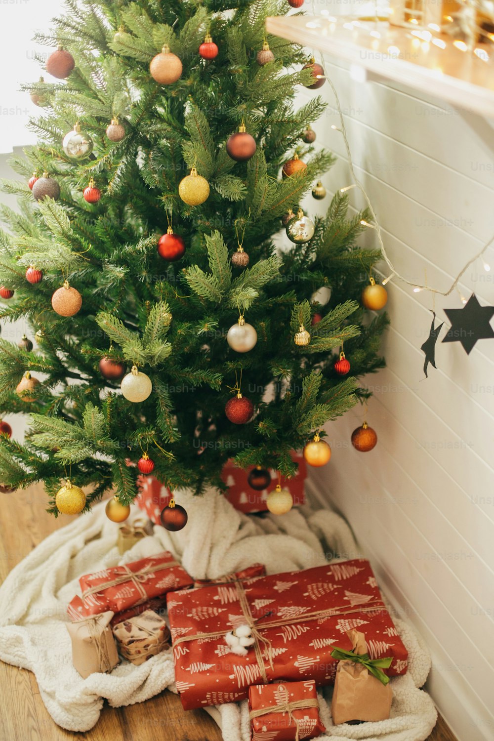 Foto Presentes de Natal elegantes sob a árvore de Natal. Caixas de presente  embrulhadas em papel moderno artesanal e árvore decorada com enfeites  vermelhos e dourados na sala escandinava festiva. Boas Festas –