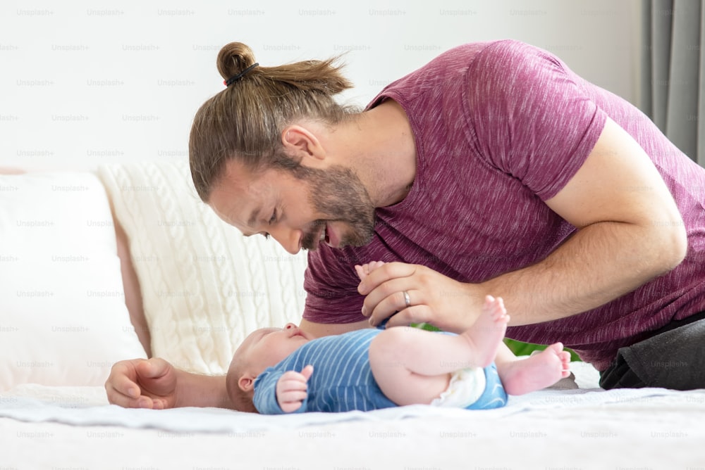 Happy Caucasian father caring and playing with newborn baby son on the bed