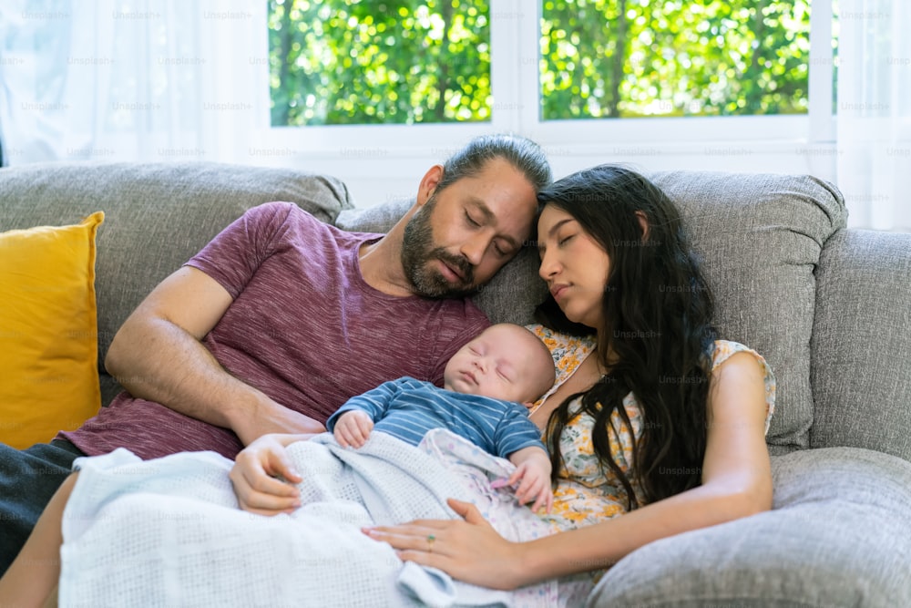 Happy family two parents with newborn baby sleeping together on sofa in living room