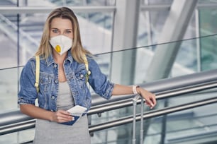 Atractiva mujer de pelo largo con máscara protectora y sosteniendo la tarjeta de embarque en la mano derecha mientras espera el vuelo