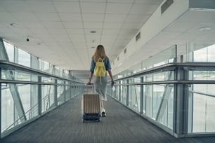 Young sporty woman pulling her suitcase while passing the corridor, having rucksack on her back