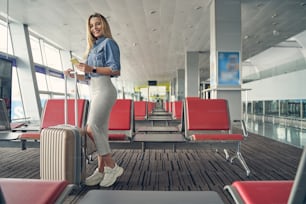 Beautiful female person keeping smile on her face while standing in semi position near her suitcase