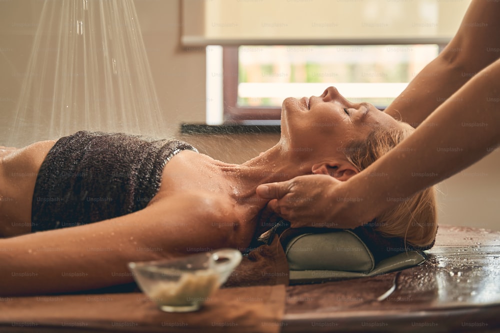 Horizontal portrait of female lying on the wooden desk while having massage in the therapist room