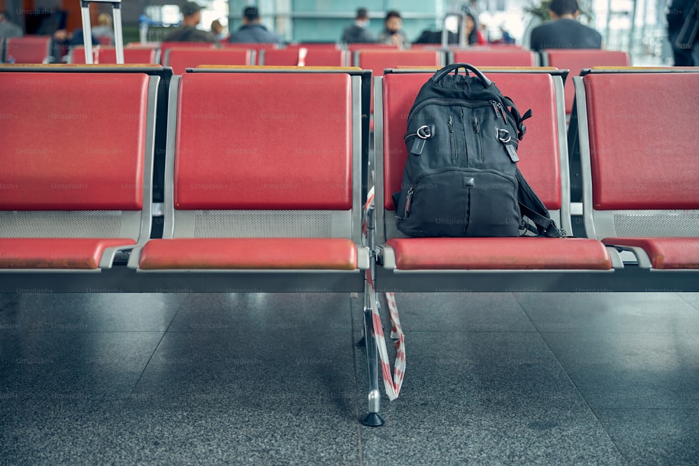 Reiserucksack wird vom Passagier auf einem roten Stuhl in der Abflughalle gelassen