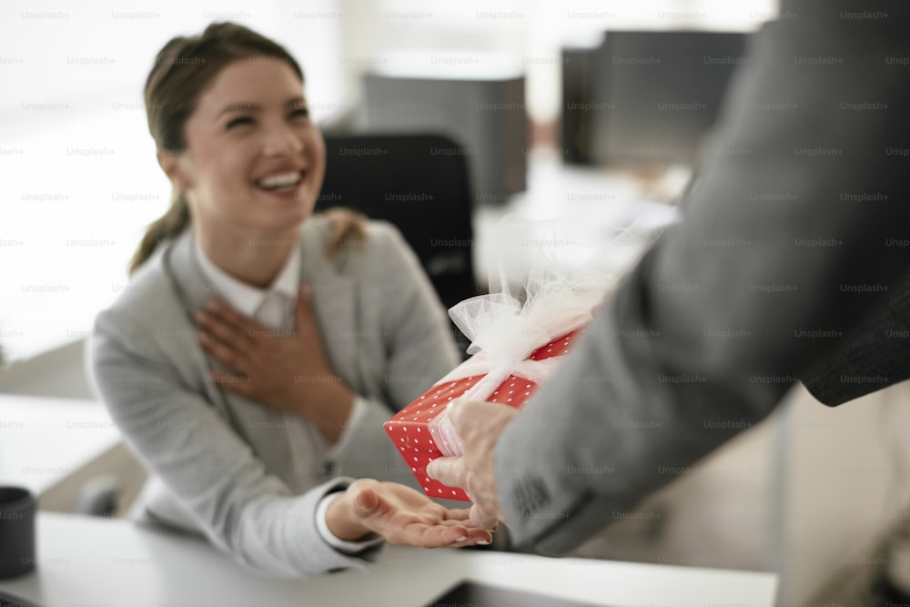 Young businessman giving his colleague present in office. Young man suprise beautiful businesswoman in office.