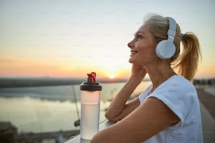 Side view of a smiling pleased modern middle-aged female in headphones enjoying her favorite songs