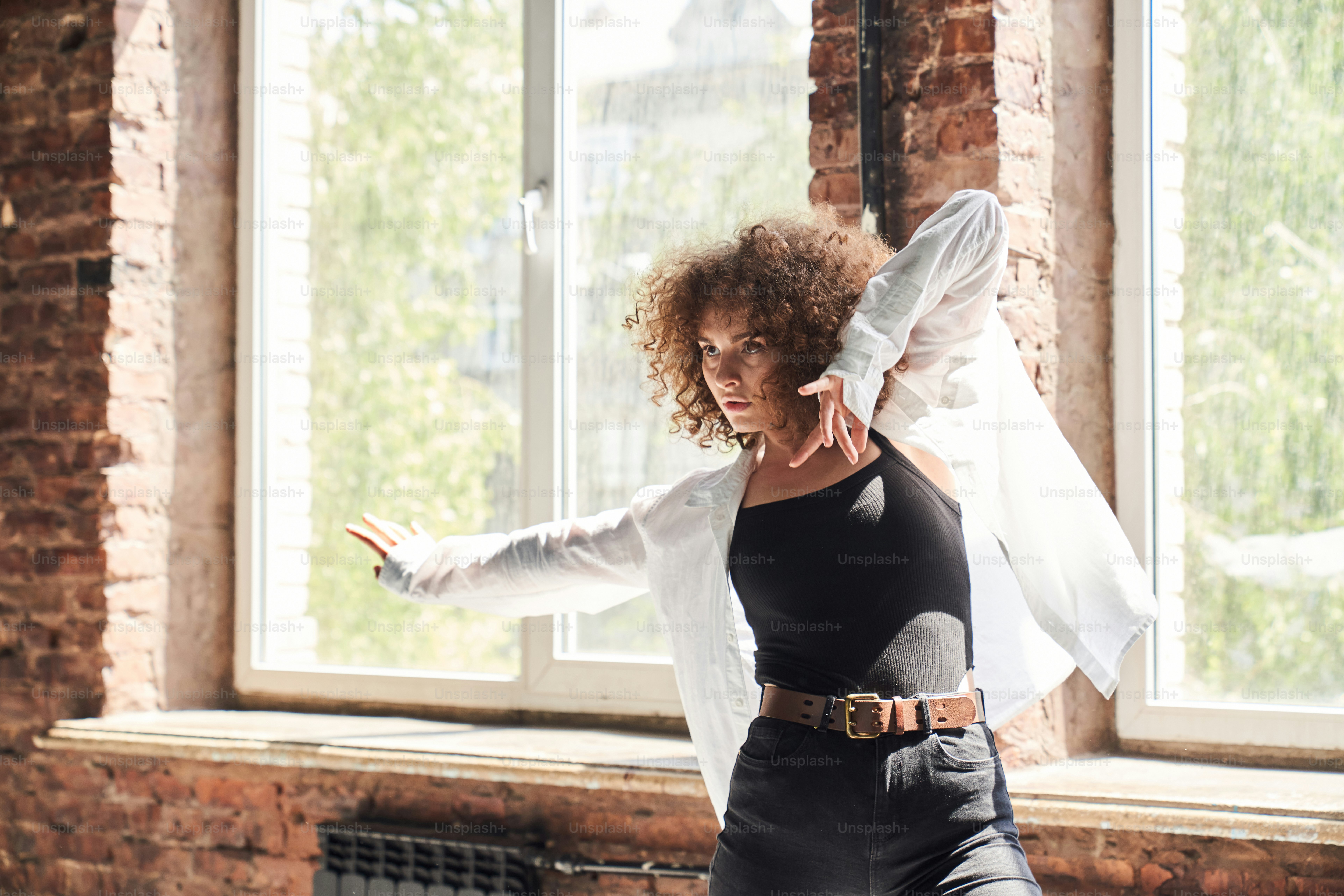 Pretty curly woman is spending free time in sport studio and practicing new movements under modern music