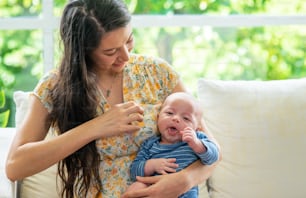 Beautiful Caucasian mother sitting on sofa with holding sleepy newborn baby son