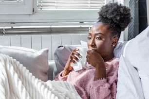 Sick day at home. African American woman has runny nose and common cold. Cough. Closeup Of Beautiful Young Woman Caught Cold Or Flu Illness. Portrait Of Unhealthy Girl Feeling Pain In Throat.