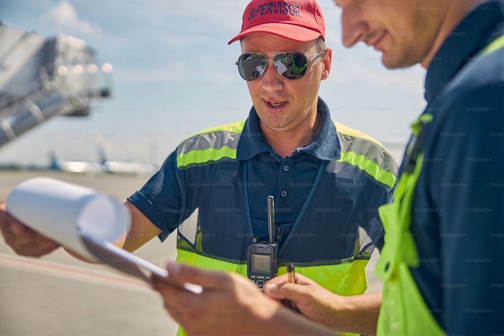 Supervisor de mantenimiento de aeronaves concentrado en ropa de trabajo mirando un documento en la mano de su colega masculino