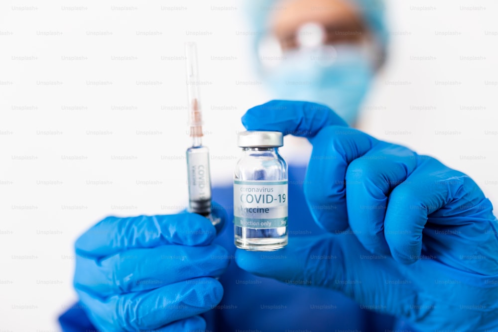 Médico, enfermera, científico, investigador mano en guantes azules sosteniendo la gripe, el sarampión, el coronavirus, la enfermedad de la vacuna covid-19 preparándose para ensayos clínicos en humanos vacuna vacuna, medicina y concepto de fármaco.