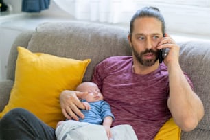 Kaukasischer Vater, der zu Hause arbeitet und sich um seinen neugeborenen Sohn kümmert.