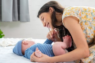 Mãe caucasiana feliz que brinca com o bebê recém-nascido na cama