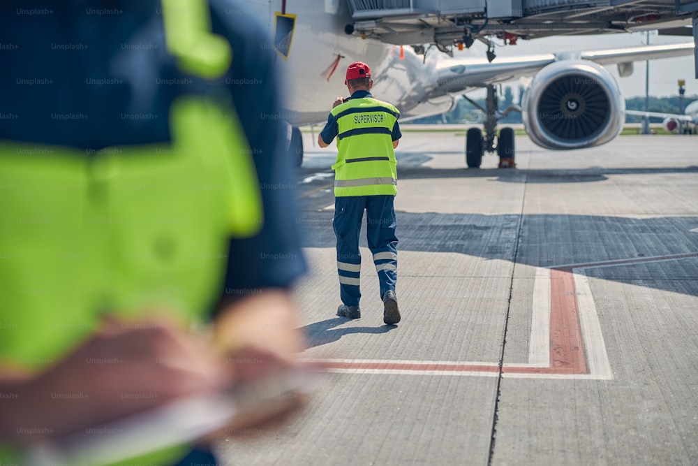Back view of an aircraft maintenance supervisor moving towards an airliner parked at the landing field