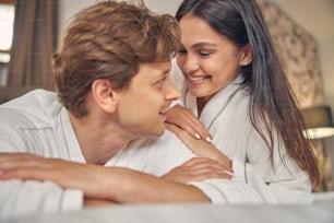 Close up portrait of romantic couple wearing white bathrobe lying in the bedroom in their house