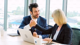 Two happy business people celebrate at office meeting room. Successful businessman congratulate project success with colleague at modern workplace while having conversation on financial data report.