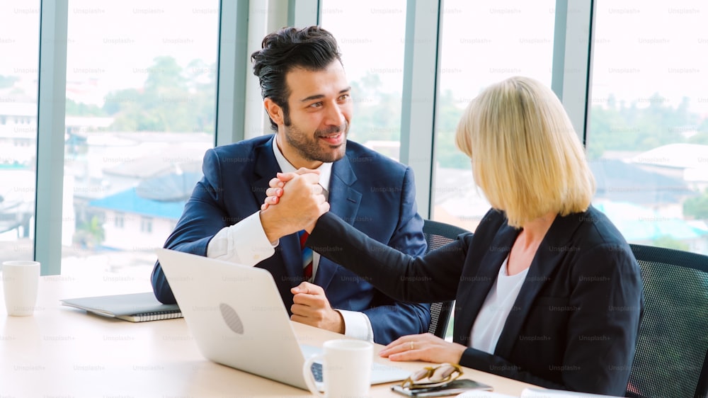 Two happy business people celebrate at office meeting room. Successful businessman congratulate project success with colleague at modern workplace while having conversation on financial data report.