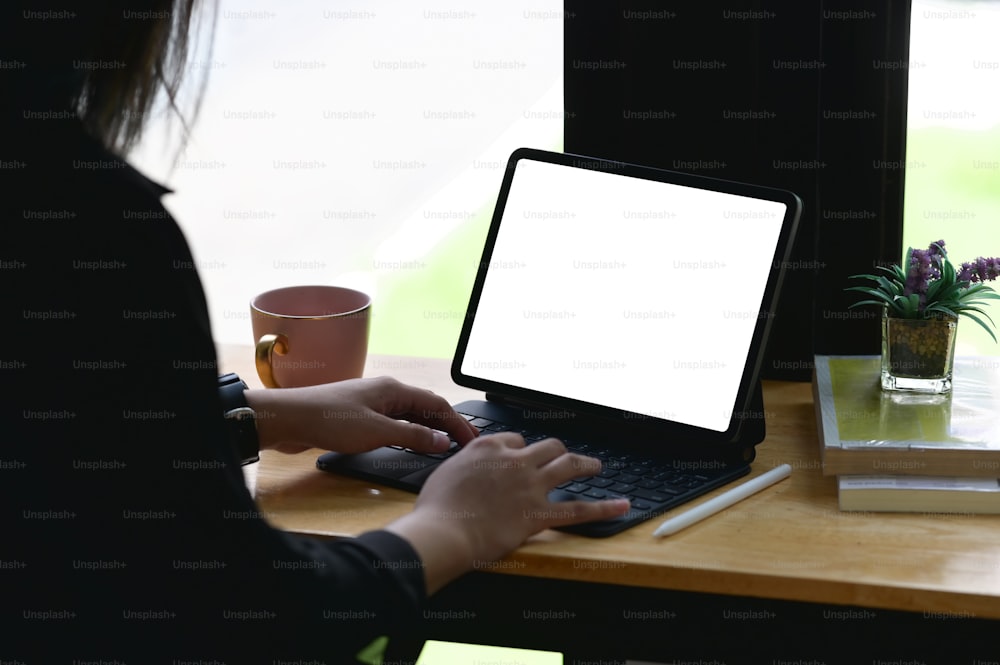 A woman is using a white blank screen tablet while sitting at the wooden table.