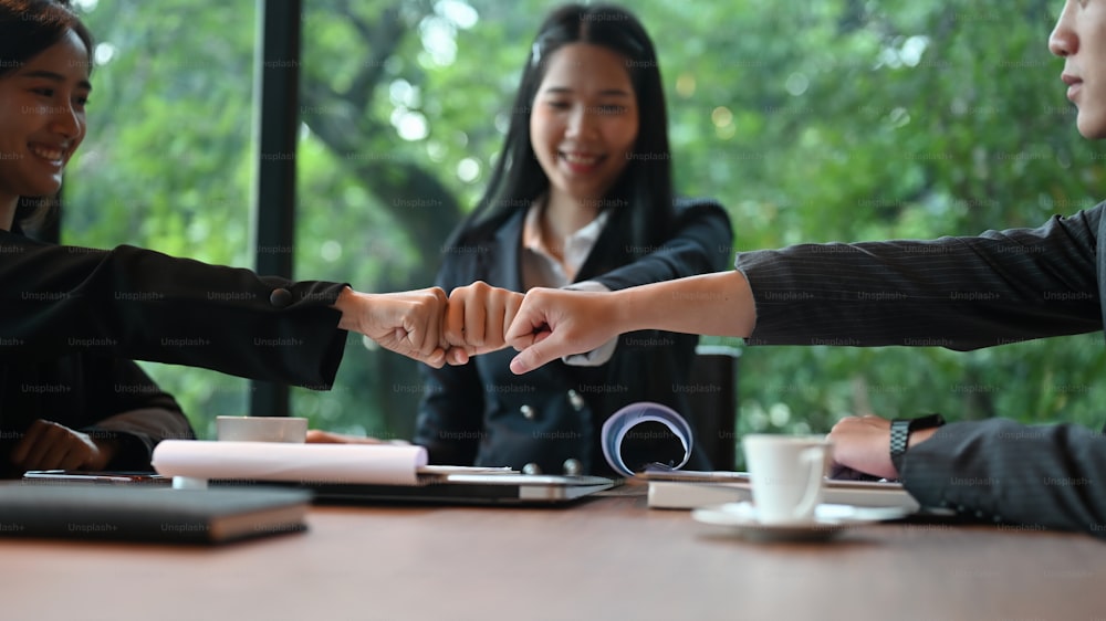 Businesspeople are greeting each other with fist-bumping while sitting at the meeting table.