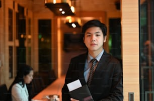 Un uomo d'affari tiene in mano un file di documenti mentre si trova sopra la sala riunioni come sfondo.