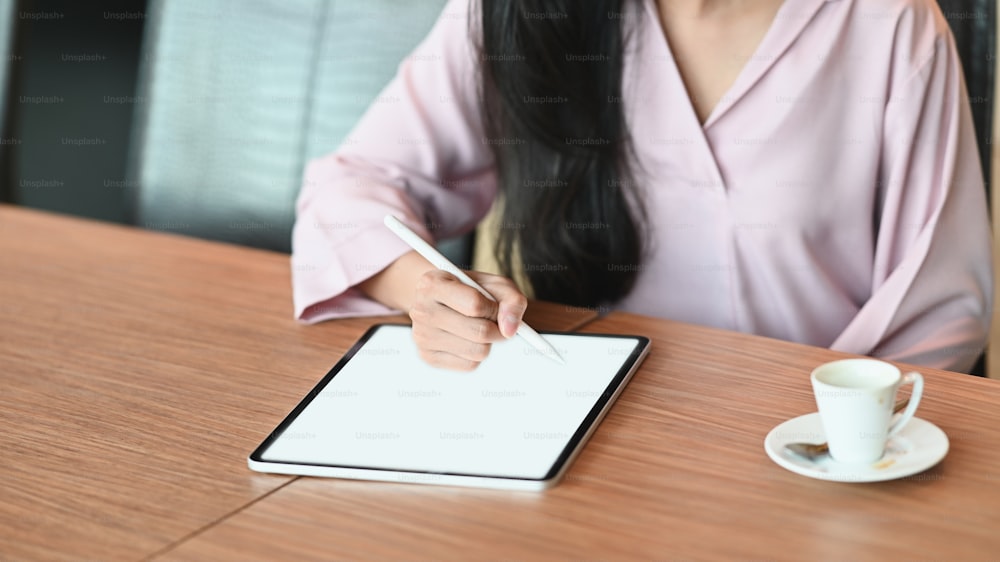Cropped image of a woman is using an empty screen tablet and stylus pen at the wooden table.