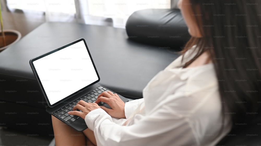 Closeup woman in pajamas is using a computer tablet on the black sofa.