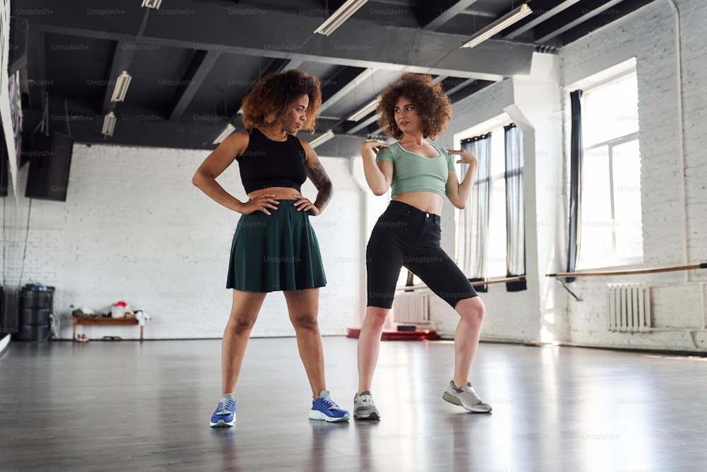 Dos bellas damas de pie en la clase de deporte mientras bailan hip-hop