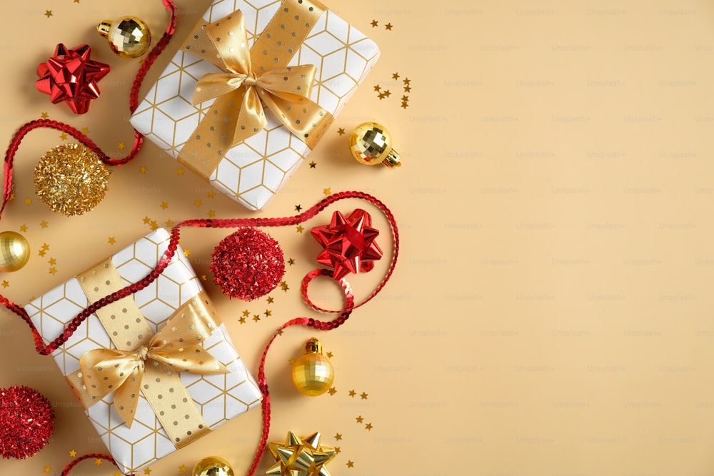 Weihnachtskomposition. Wohnung legen Weihnachtsgeschenke, rote und goldene Kugeln Dekorationen, Lametta, Konfetti auf pastellgelben Tisch. Weihnachts- und Neujahrsferienhintergrund.