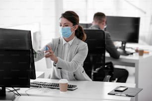 Businesswoman with medical mask disinfecting desk in the office.