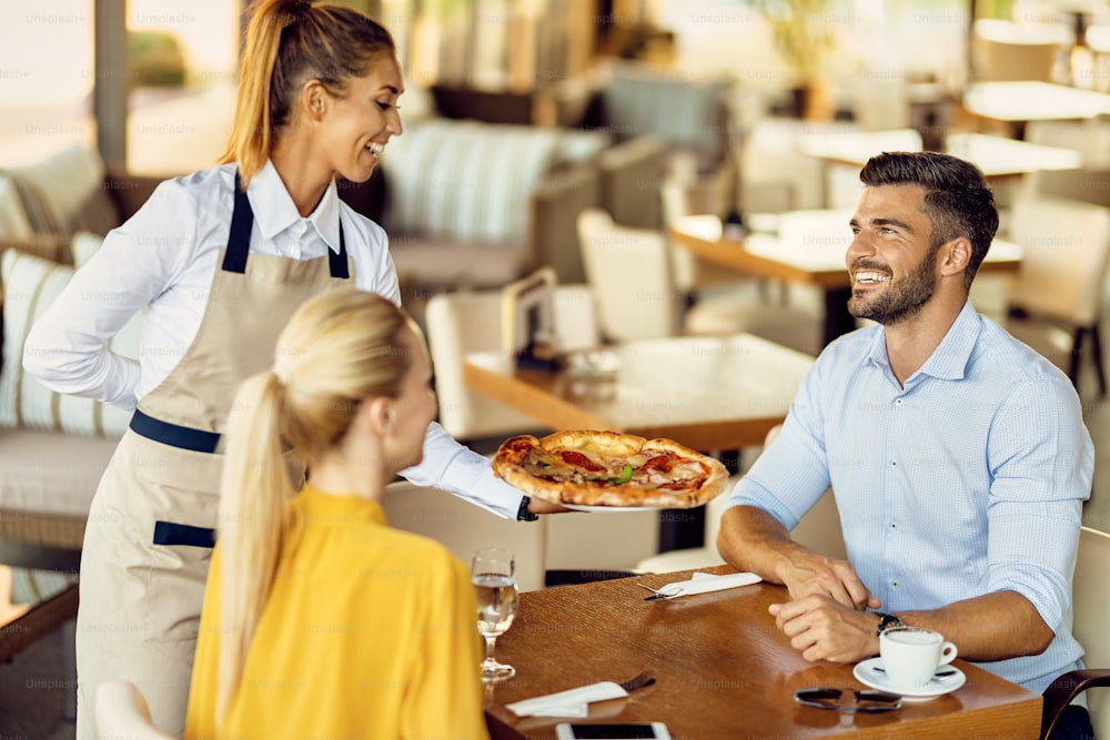 Happy couple enjoying in restaurant while waitress is serving the pizza. Focus is on man.