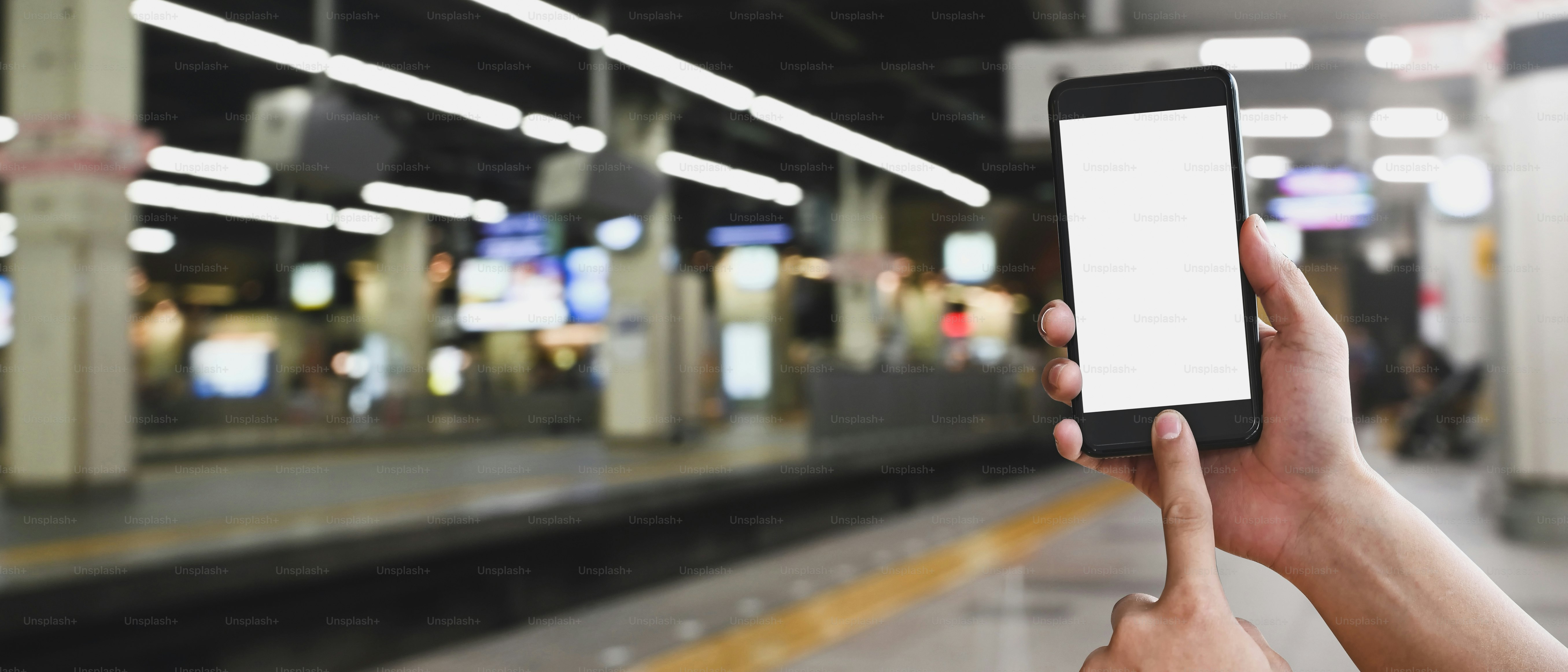 Cropped image of hands is using a white blank screen smartphone at the subway.