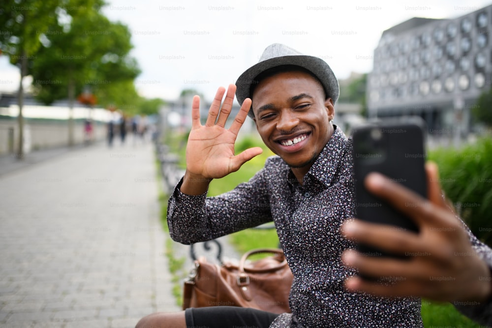 Cheerful black man commuter sitting on bench outdoors in city, video call concept.