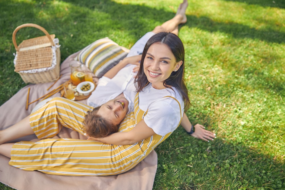 Mujer sonriente con su hombre encantador descansando en el picnic en el bosque verde en el día del sol