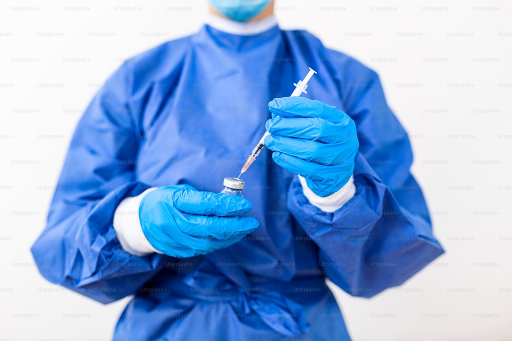 PPEスイートの制服を着た女性の医師または科学者の接写の手実験室で保護するフェイスマスクを着用し、薬の液体ワクチンバイアルボトルと注射器、コロナウイルスまたはCOVID-19のコンセプト白を分離