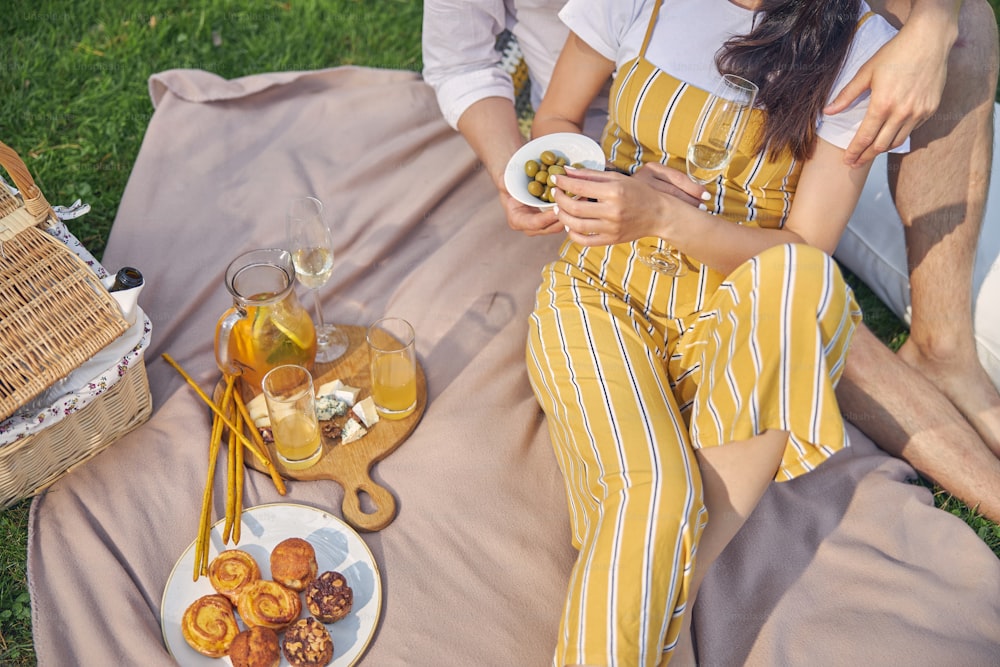 Top view of wooden old plate with cheese and orange lemonade standing near the woman in yellow overalls