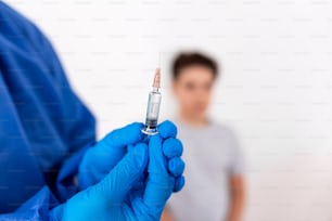 Vaccination. Professional doctor in blue sterile gloves holding syringe and making injection to a little boy wearing medical mask. Immunisation, medicine and healthcare. Covid19, coronavirus vaccine