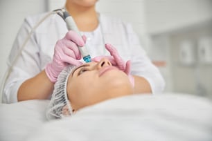 Frau liegt still während eines dermatologischen Eingriffs, der von einer Kosmetikerin in einem Schönheitssalon durchgeführt wird