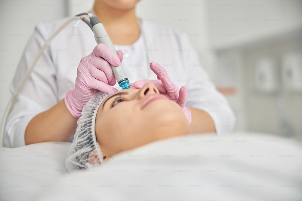 Donna sdraiata immobile durante una procedura dermatologica eseguita da un'estetista in un salone di bellezza