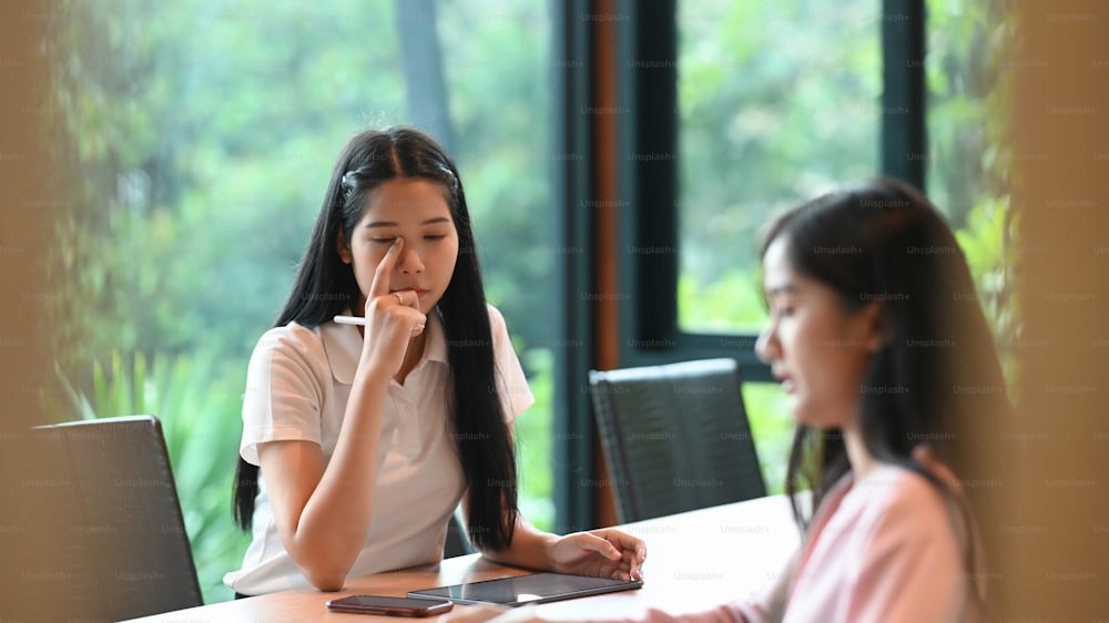 A beautiful woman is using a computer tablet and stylus pen while sitting in the meeting room.