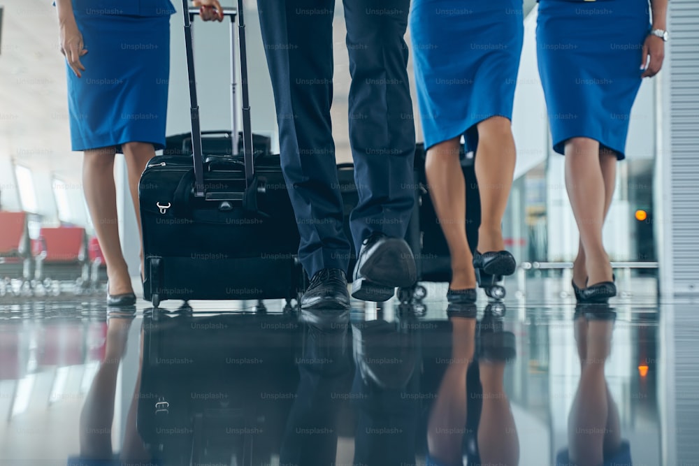 Foto recortada de jóvenes auxiliares de vuelo caucásicos con zapatos de moda caminando por la terminal del aeropuerto