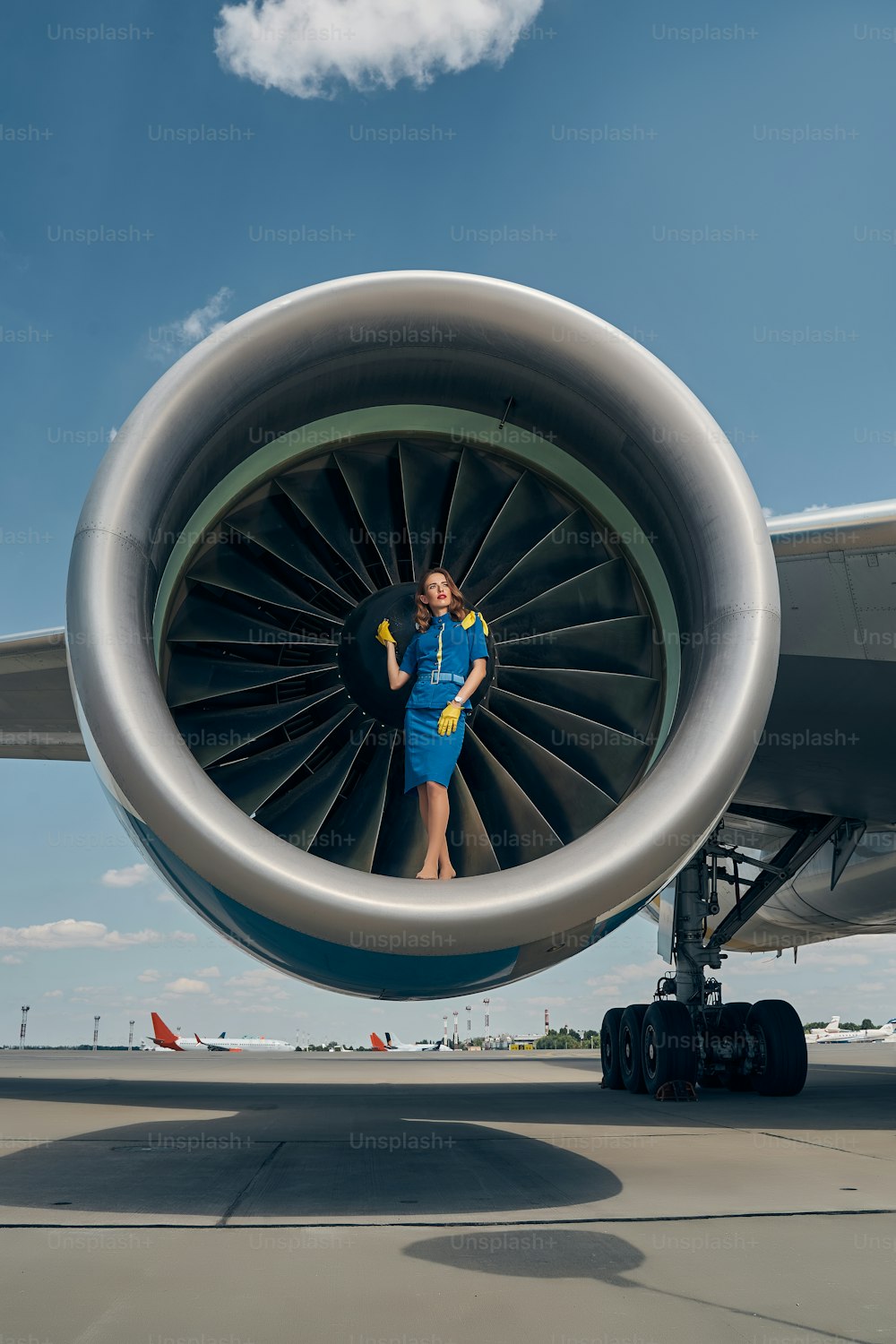 Full-length portrait of a thoughtful young Caucasian flight attendant leaning against the jet engine spinner