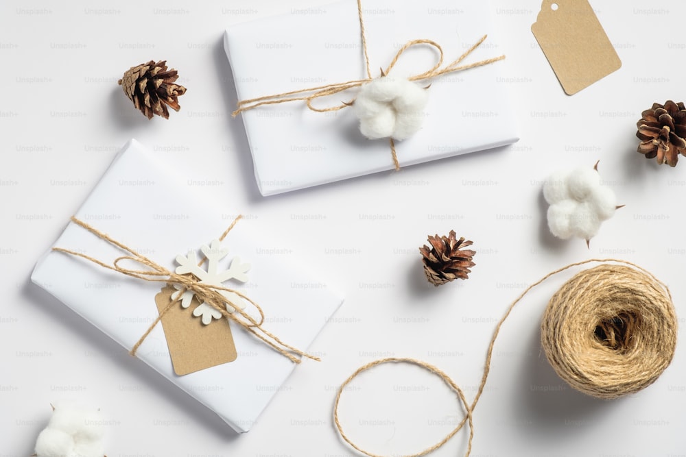 Vintage Christmas flat lay composition. Handmade gift boxes, twine, cotton and pine cones on white background. Retro style